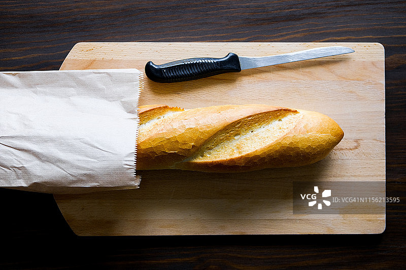 纸袋装新鲜面包、餐刀和木制案板特写，留白图片素材