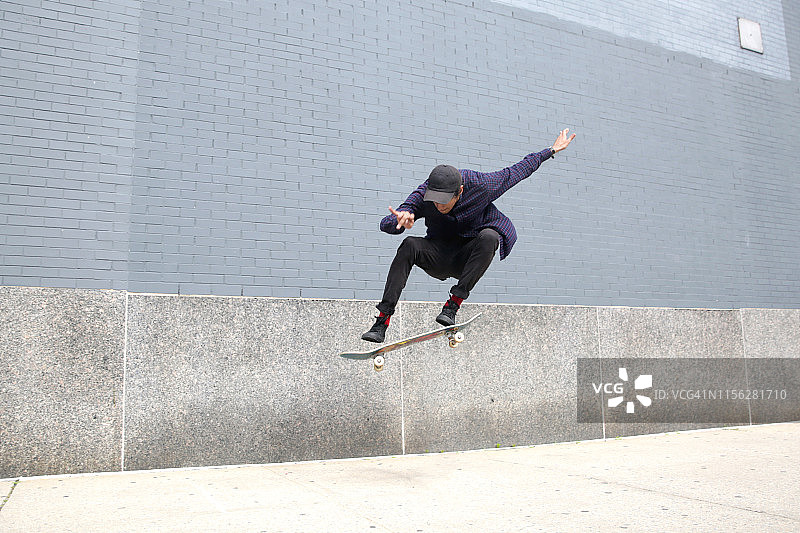 年轻的混血千禧一代男性在纽约市一栋建筑物前玩滑板图片素材