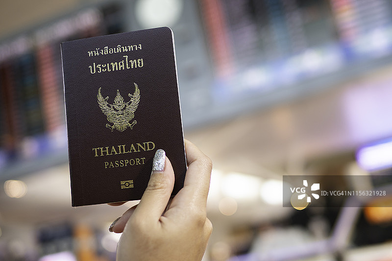 旅行度假概念：手持泰国护照，背景为机场航班时刻表图片素材