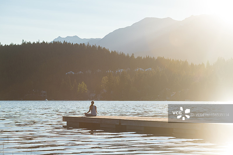 女人在山间湖泊的码头上冥想图片素材