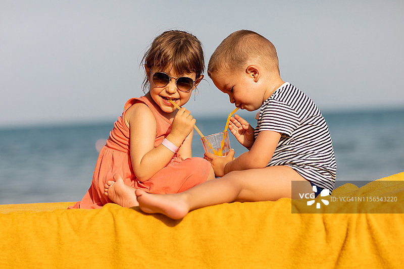 在海滩上一起喝果汁的快乐儿童图片素材
