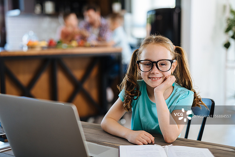 在笔记本电脑上做作业的微笑小女孩图片素材