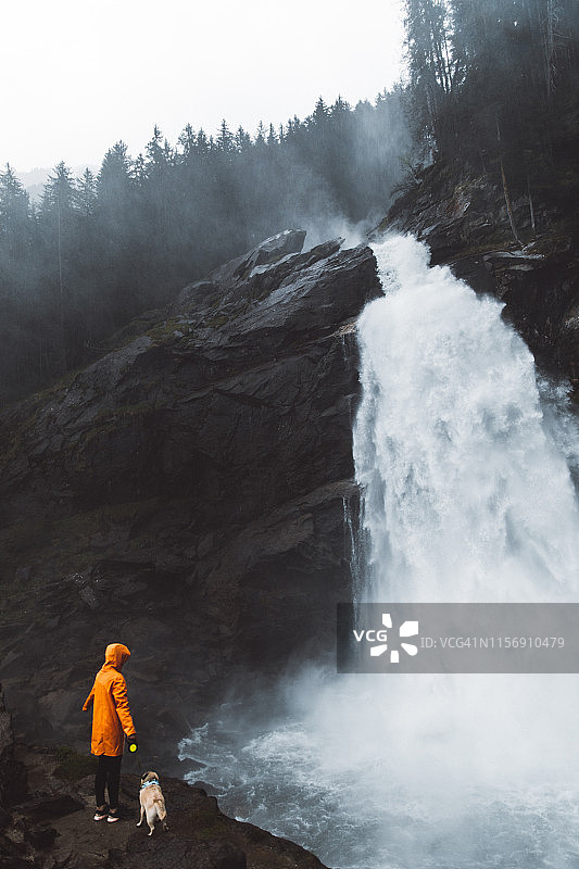 身穿雨衣，带着狗，看着奥地利阿尔卑斯山克里姆尔瀑布的女人图片素材