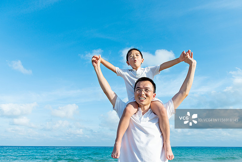 儿子坐在父亲的肩膀上享受海滩图片素材