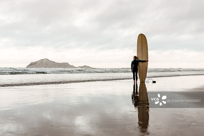 站在海滩上冲浪板旁边的少女图片素材