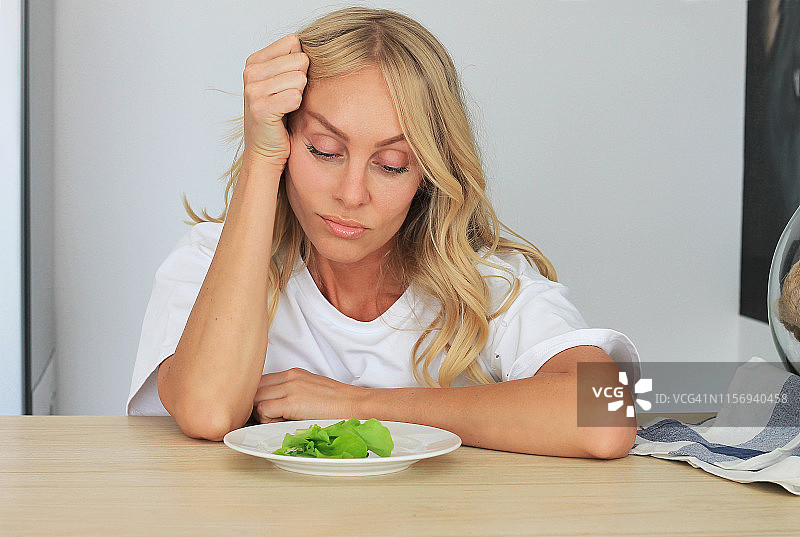 我厌倦了难吃的沙拉，不高兴的女士看着一盘生菜图片素材