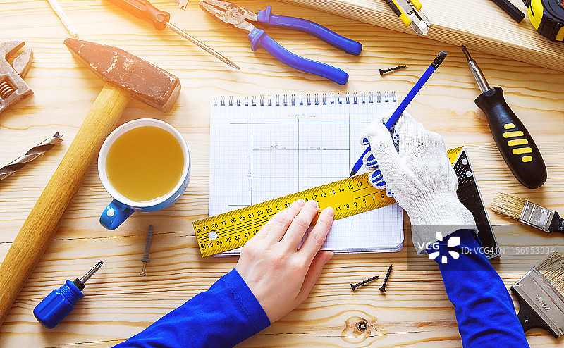 木匠在木桌上绘制建筑或维修项目图纸，旁边放着一杯茶和建筑工具，工头的工作场所，家庭和专业维修图片素材
