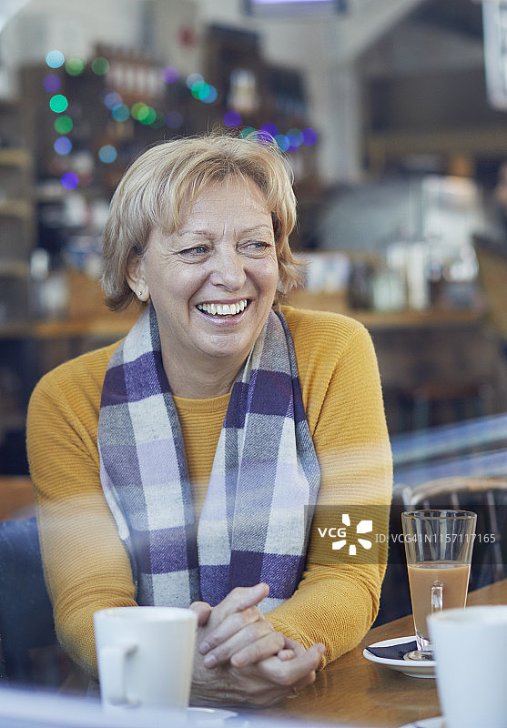 微笑的中年妇女在咖啡馆的桌旁喝咖啡图片素材