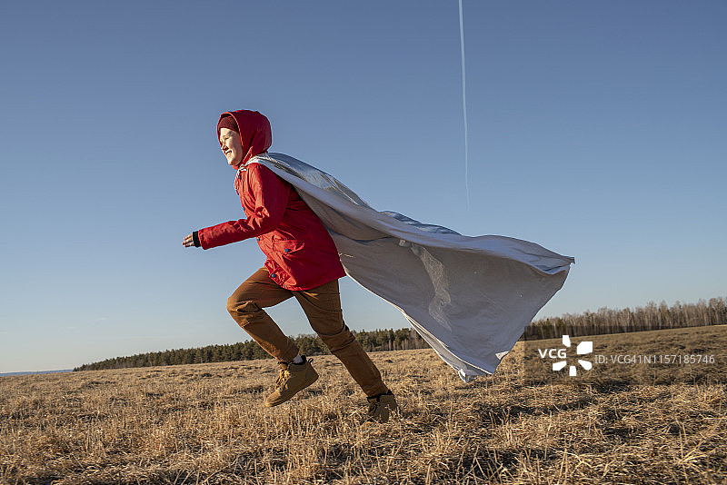 装扮成超级英雄在草原上奔跑的男孩图片素材