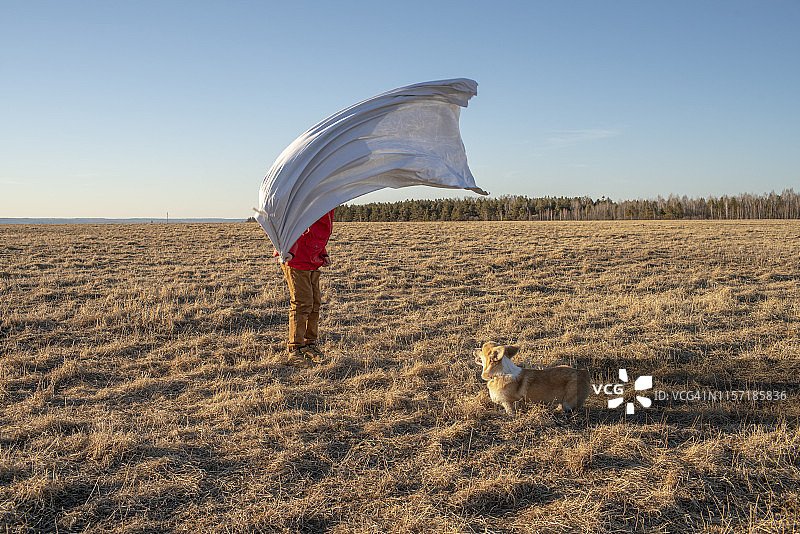狗和穿着超级英雄服装的男孩在草原景观中图片素材