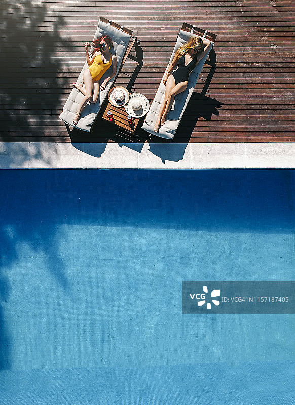 两位美丽女人在泳池边的露台上晒日光浴图片素材