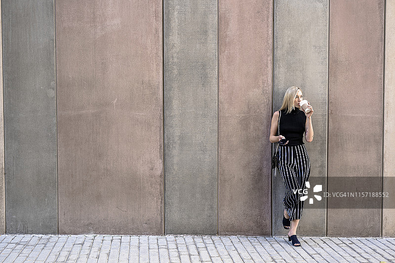 靠墙喝咖啡的金发年轻女人图片素材