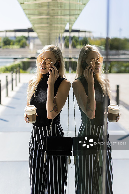 拿着咖啡打电话的金发年轻女人图片素材