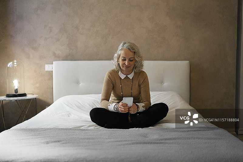坐在床上使用手机的年长的女商人肖像图片素材