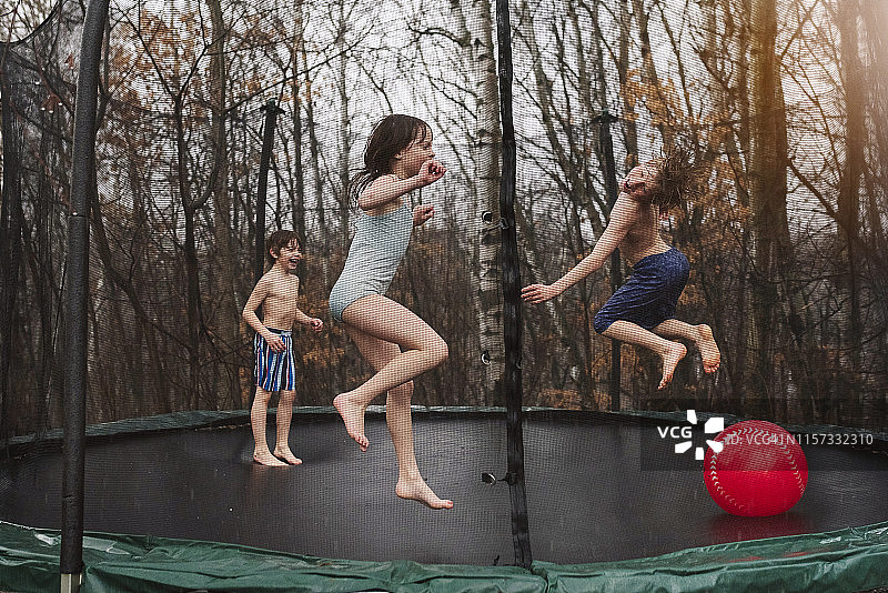 三个孩子在雨中在蹦床上跳跃图片素材