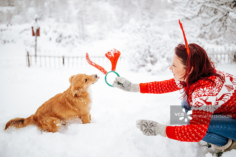 女人和狗戴着驯鹿角享受雪景图片素材