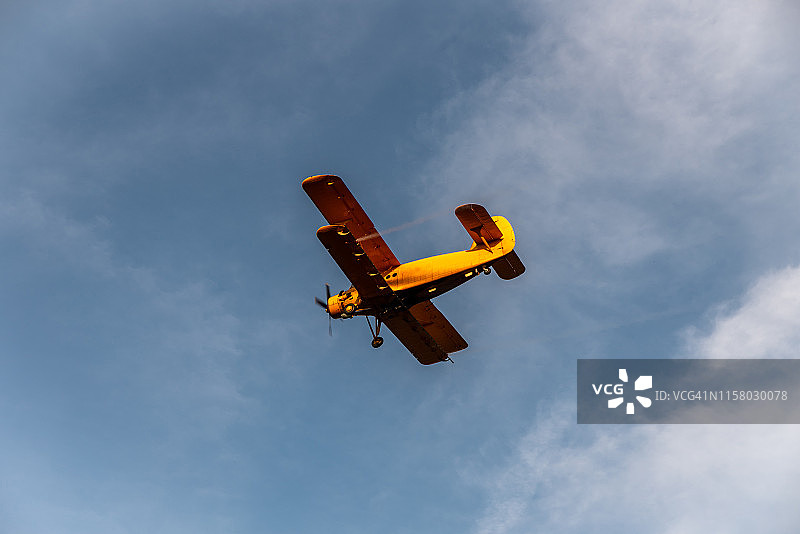 傍晚，橙色小型双翼飞机在农田上喷洒农药和除草剂，防治病虫害图片素材