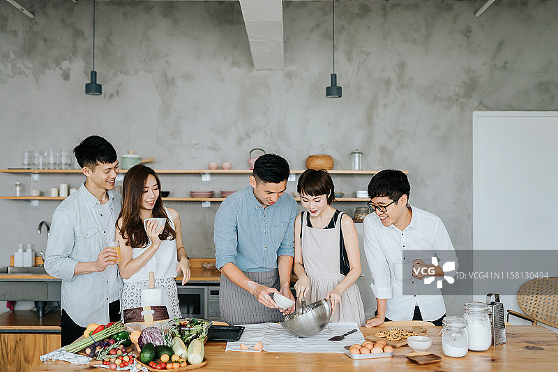快乐的亚洲年轻男人和女人在现代厨房一起做饭，一边聊天一边为聚会准备食物图片素材