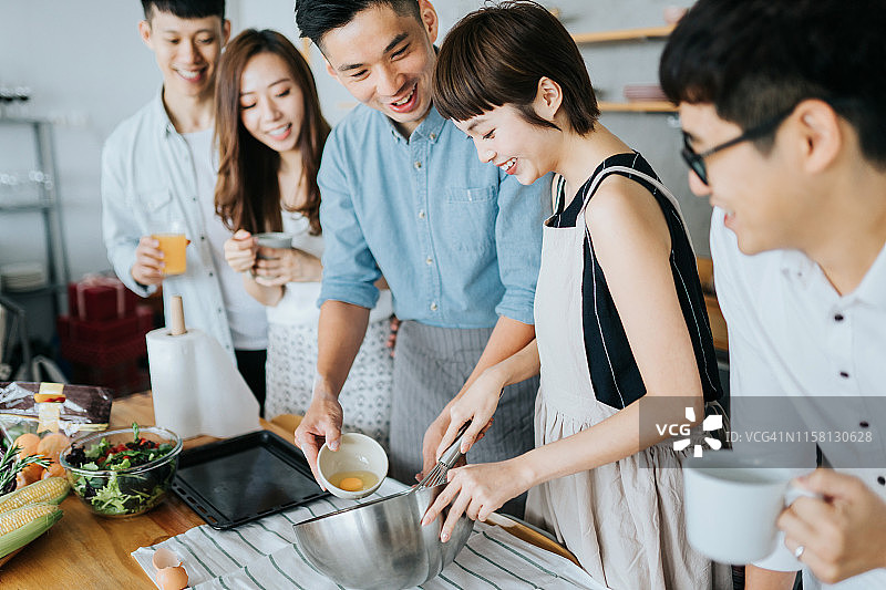 快乐的亚洲年轻男人和女人在现代厨房一起做饭，一边聊天一边为聚会准备食物图片素材