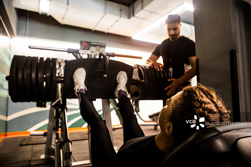 在健身俱乐部，男私人教练指导女性进行腿举训练图片素材