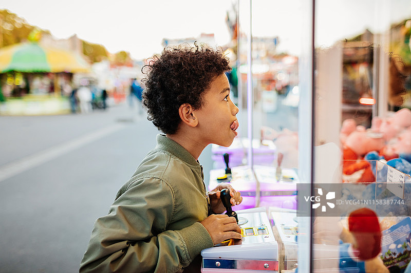 在游乐场抓娃娃机上赢奖品的男孩图片素材