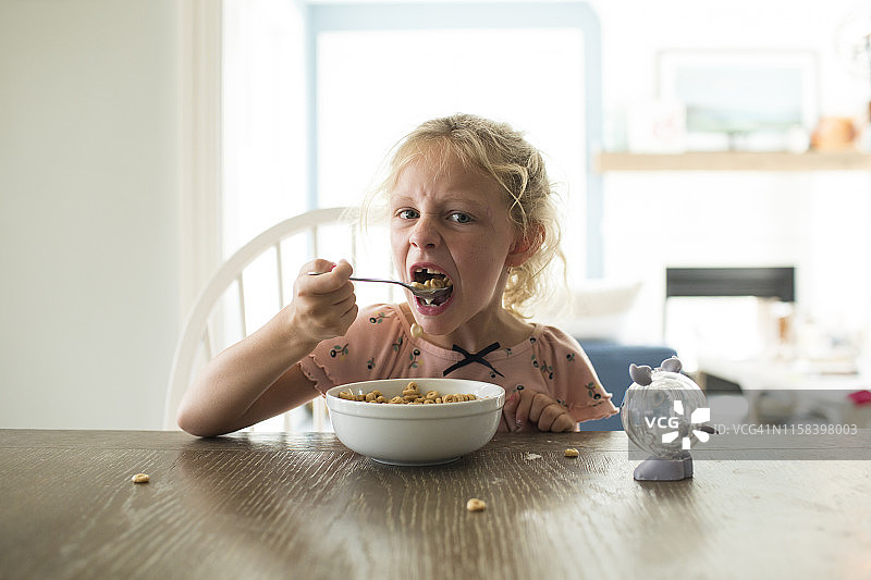 在明亮的厨房餐桌旁吃麦片的掉牙金发女孩图片素材