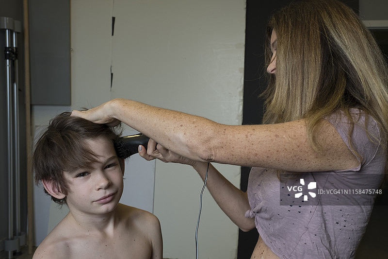 在工作室里，一位母亲用理发器给儿子剃头的中景特写镜头图片素材