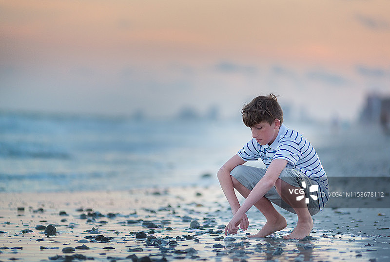 蹲在海边沙滩上的男孩图片素材