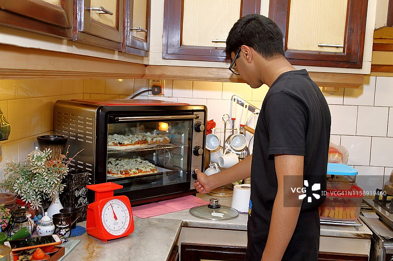 青少年男孩在烤箱里烤披萨图片素材