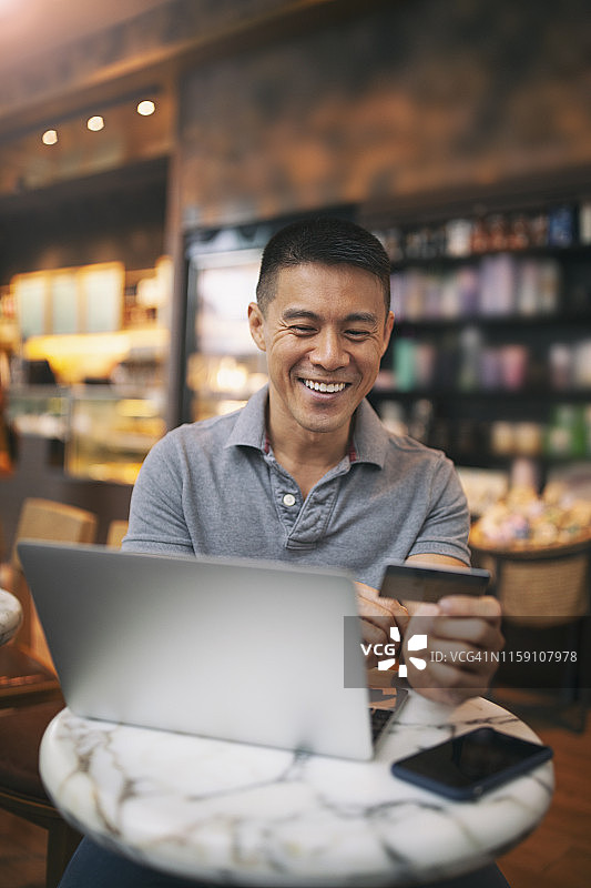 亚洲英俊男子在咖啡馆用笔记本电脑进行在线支付图片素材