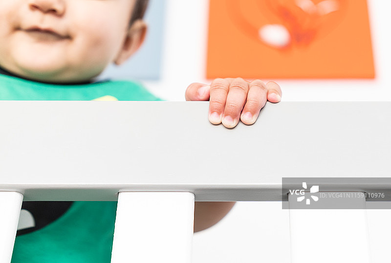 婴儿站立并扶着婴儿床栏杆的手部特写图片素材