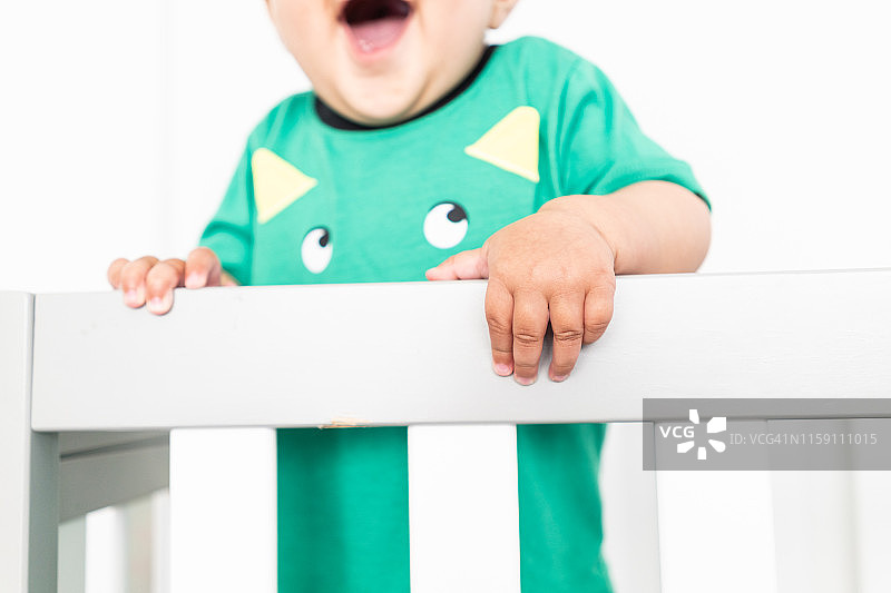 婴儿站立并扶着婴儿床栏杆的手部特写图片素材