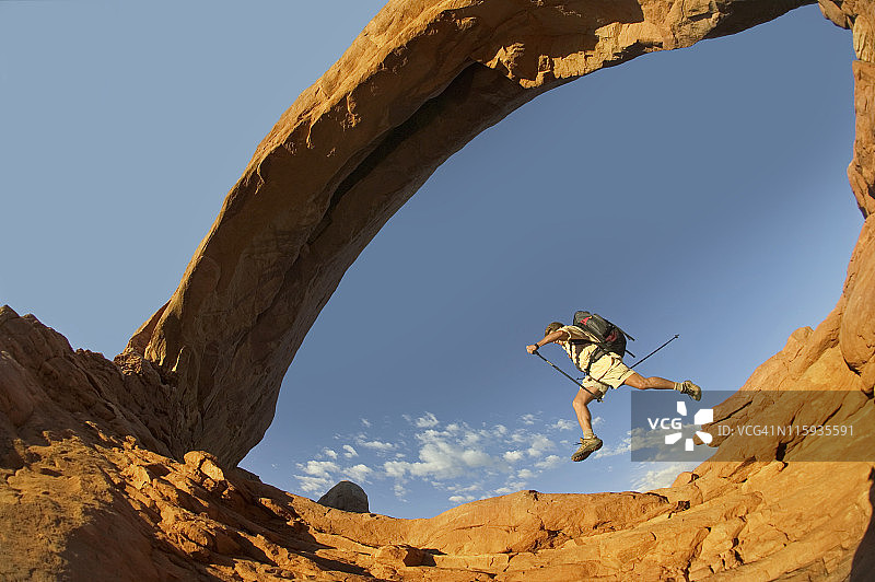 徒步旅行者从拱门下的岩石上跳跃图片素材