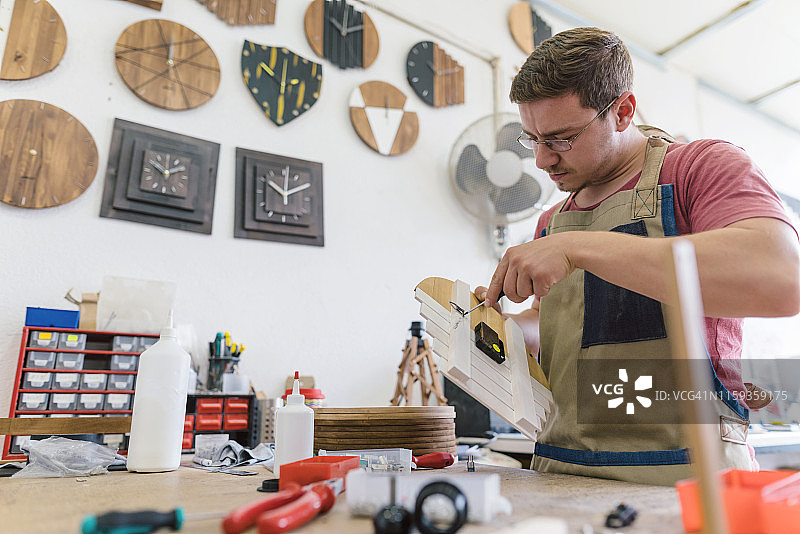 组装木制挂钟的年轻工匠图片素材