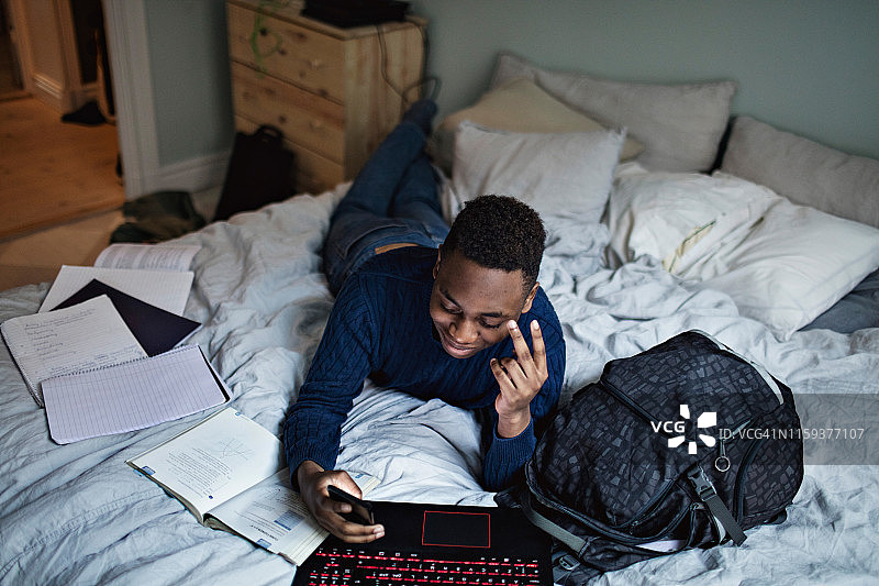 微笑的青少年在家在床上做作业时使用社交媒体图片素材