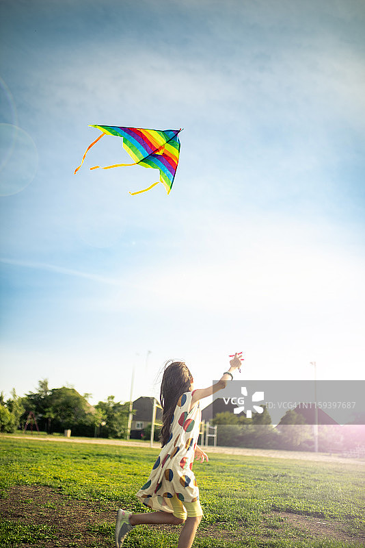 快乐的女孩在夕阳下放飞彩色风筝图片素材