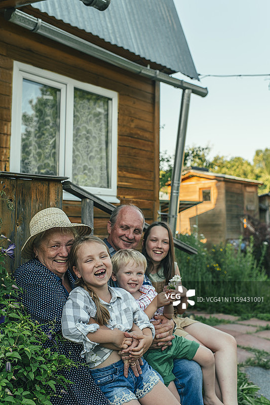 夏日里，祖父母和孙子孙女坐在房子旁图片素材
