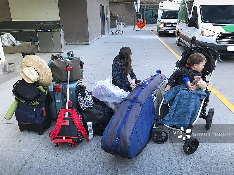 母亲和坐在婴儿车里的年幼男孩在机场堆放着大量行李图片素材