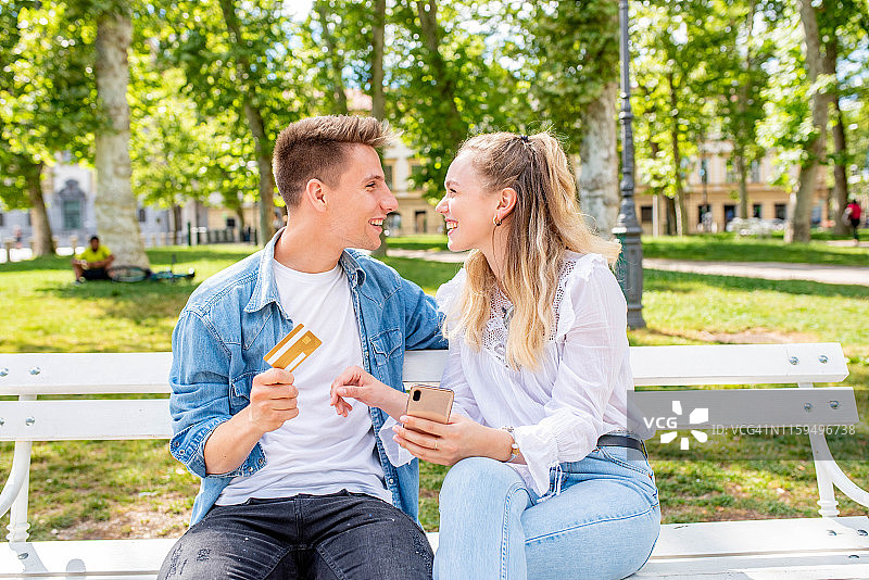 年轻情侣在公园里使用手机和信用卡图片素材