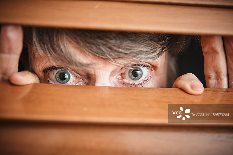 透过百叶窗紧张地凝视的年长妇女图片素材