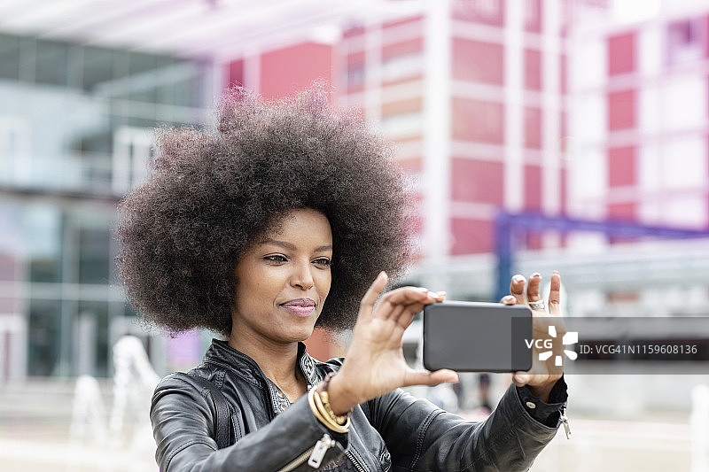 在城市火车站有非洲发型的年轻女人，正在用智能手机自拍图片素材