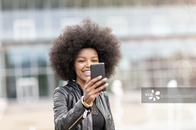 非裔发型年轻女子在城市广场用手机自拍图片素材