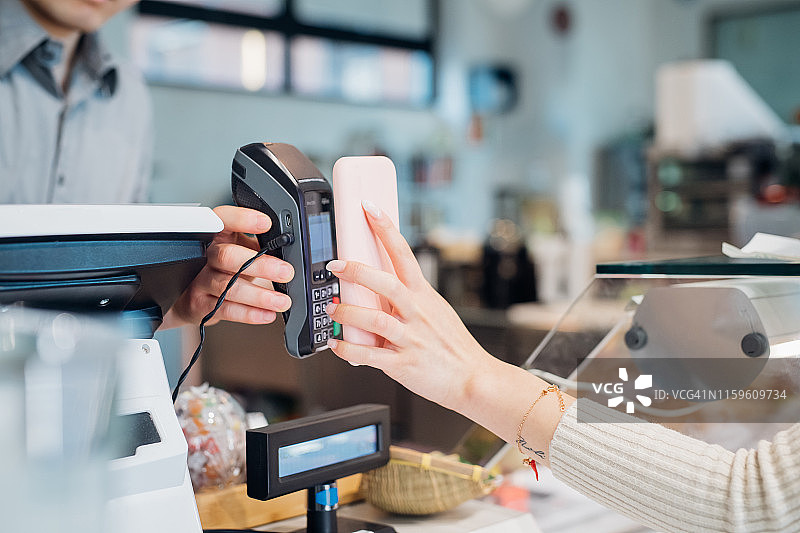年轻女商人在咖啡馆柜台用智能手机付款（局部）图片素材