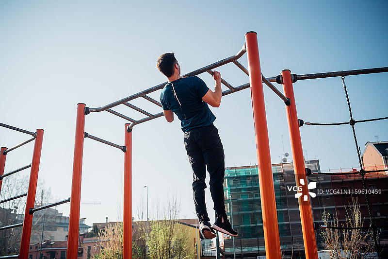 在户外健身房进行健美运动，年轻男子在运动器材上做引体向上，后视图图片素材