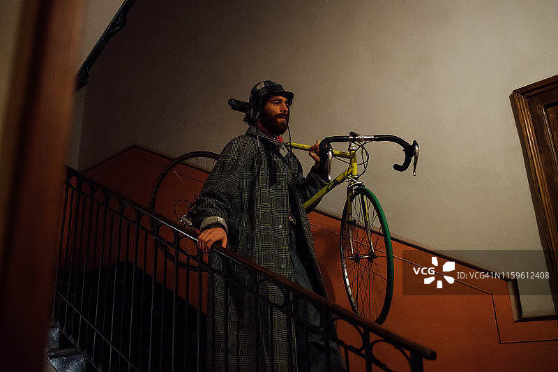 肩扛自行车走下楼梯的年轻络腮胡男子图片素材