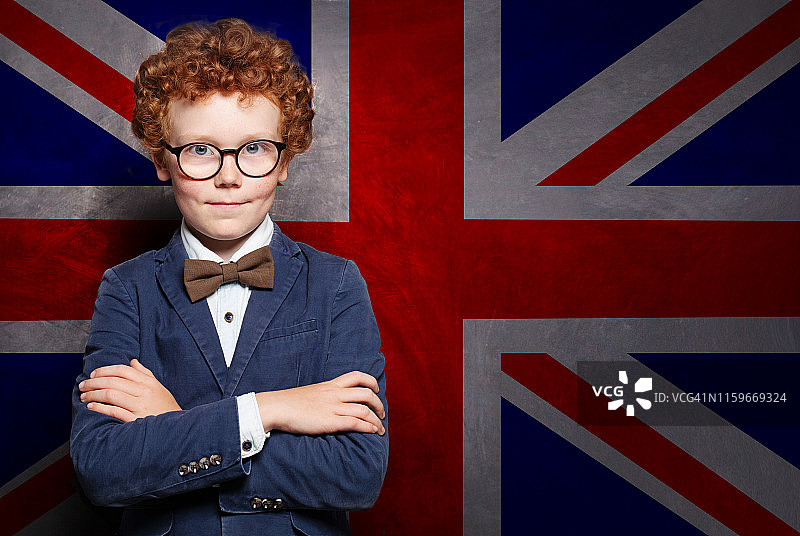 穿着西装、戴着眼镜的聪明孩子，背景是英国国旗。英语学校概念图片素材