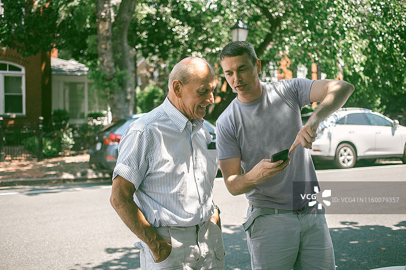 年轻人向年长的男人展示最新的智能手机应用图片素材