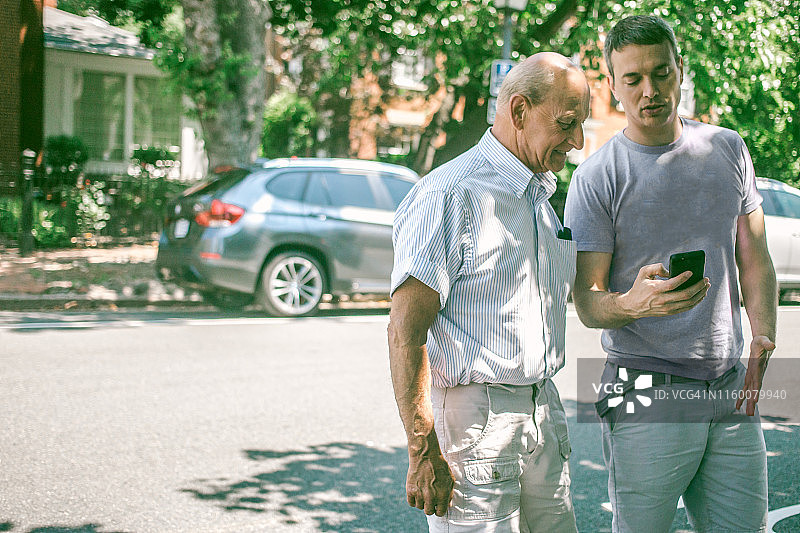 年轻人向年长的男人展示最新的智能手机应用图片素材