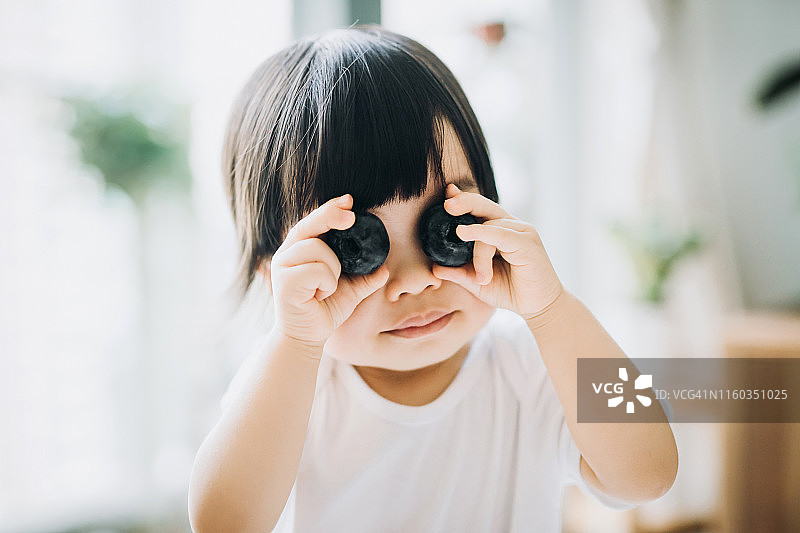 快乐的亚洲小女孩拿着大蓝莓遮住眼睛图片素材