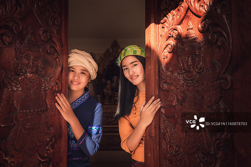 身穿泰国兰纳和掸族传统服装的亚洲女性站在雕刻艺术木门前的肖像图片素材